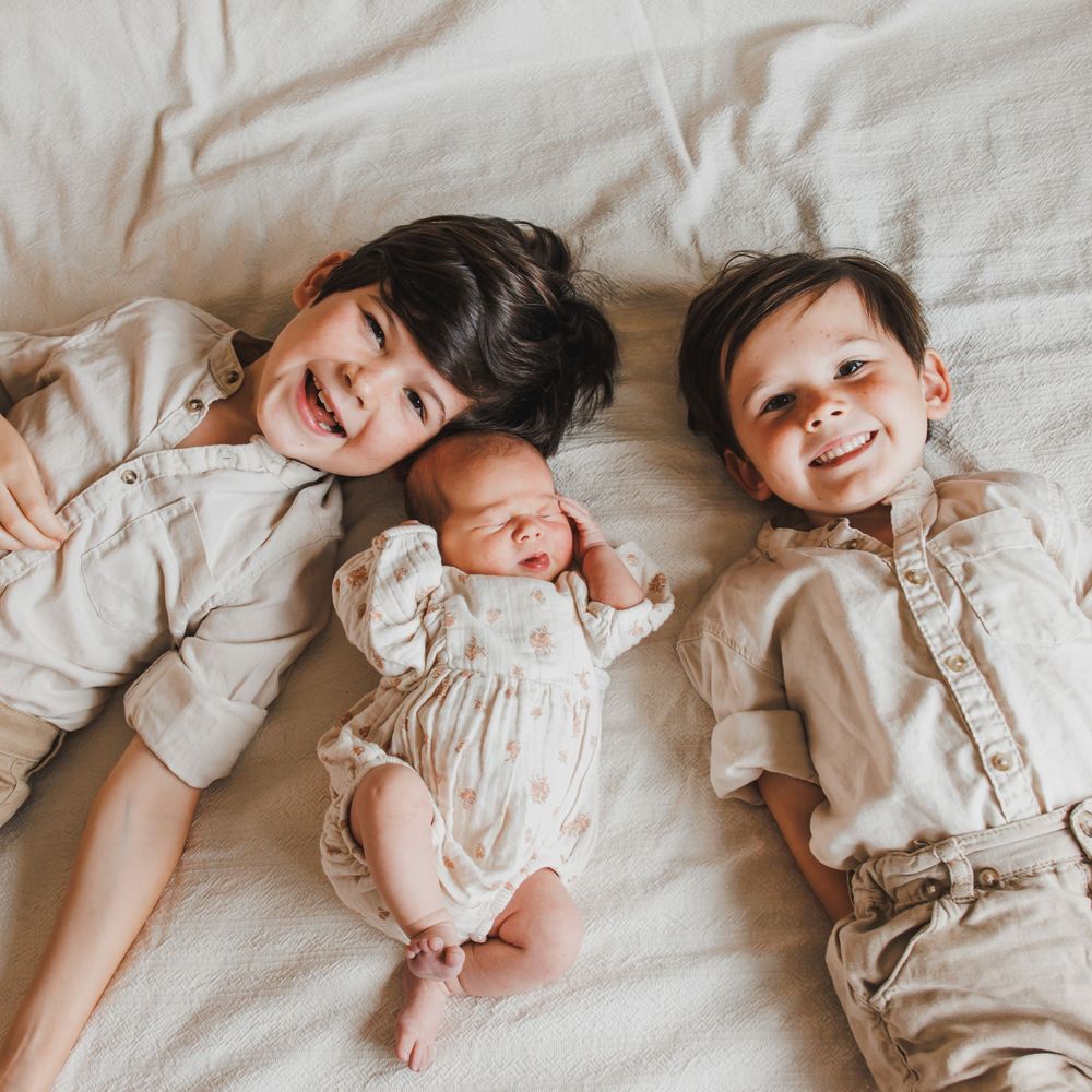 3 siblings together lying on bed with heads touching.