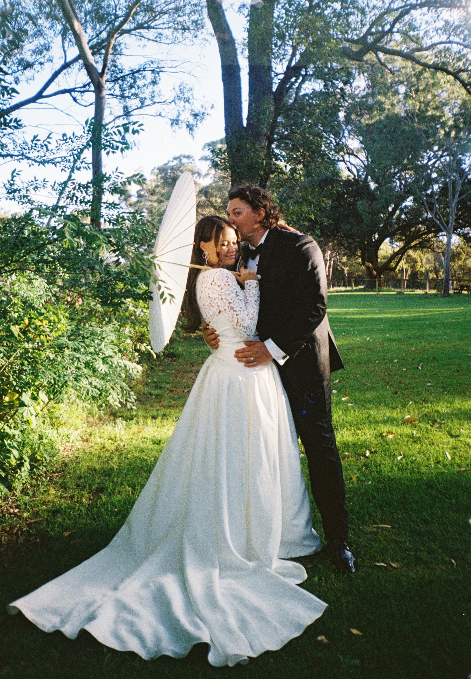 A romantic outdoor wedding photoshoot featuring a couple in formal attire posing in a lush green park setting.
