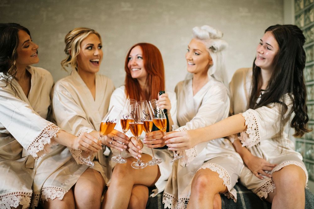 Bridal party in matching robes celebrates with champagne during morning preparations.