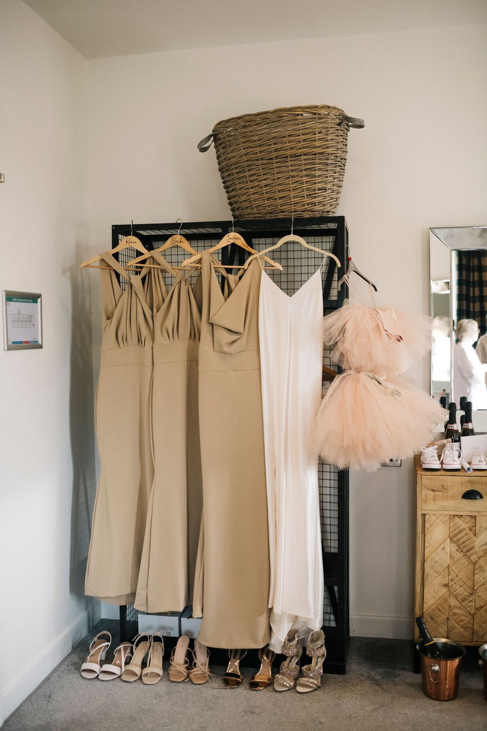 Wedding dresses and bridesmaids gowns hanging neatly on a wall with wicker baskets above.