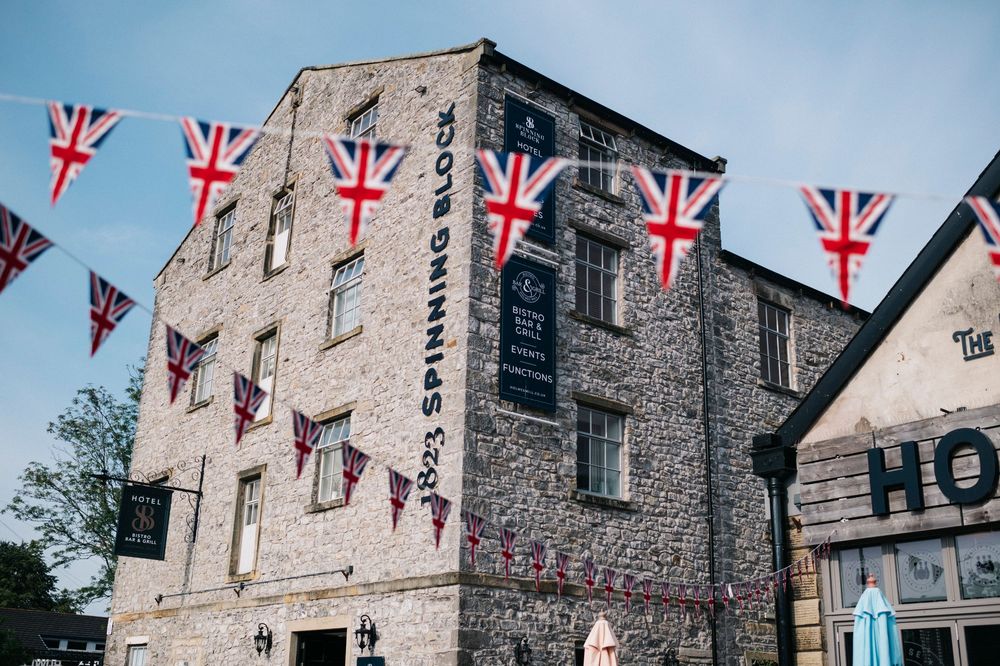 Stone buildings decorated with Union Jack bunting and flags line a historic street.