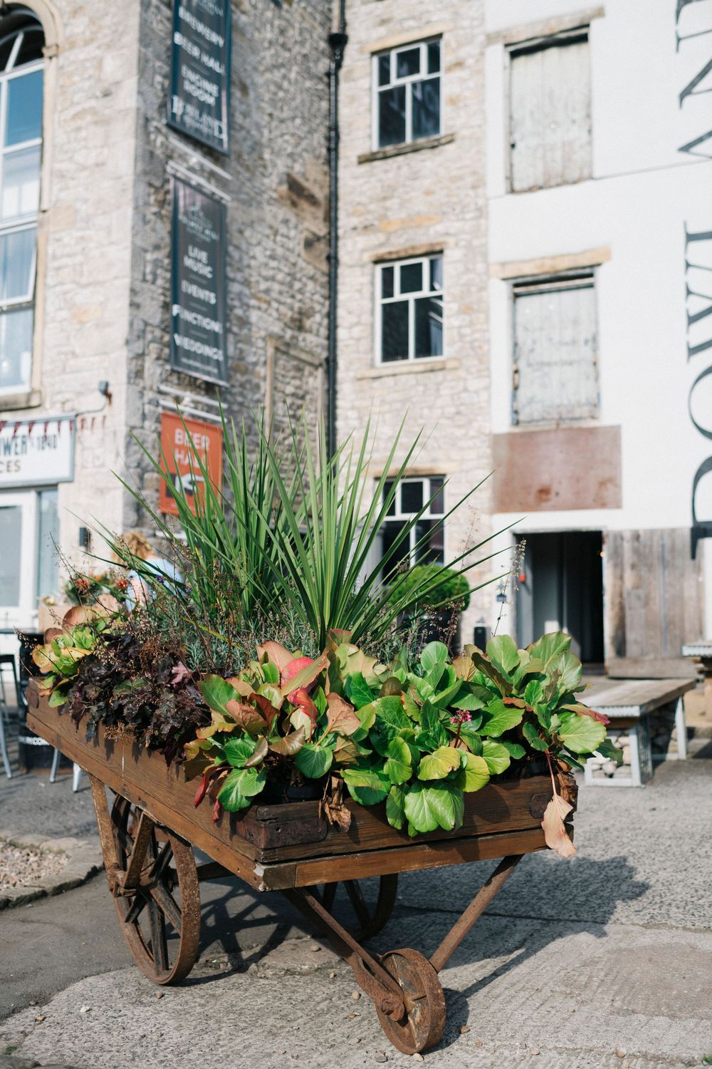 Rustic wooden wheelbarrow planters filled with greenery and flowers displayed against stone building exterior.