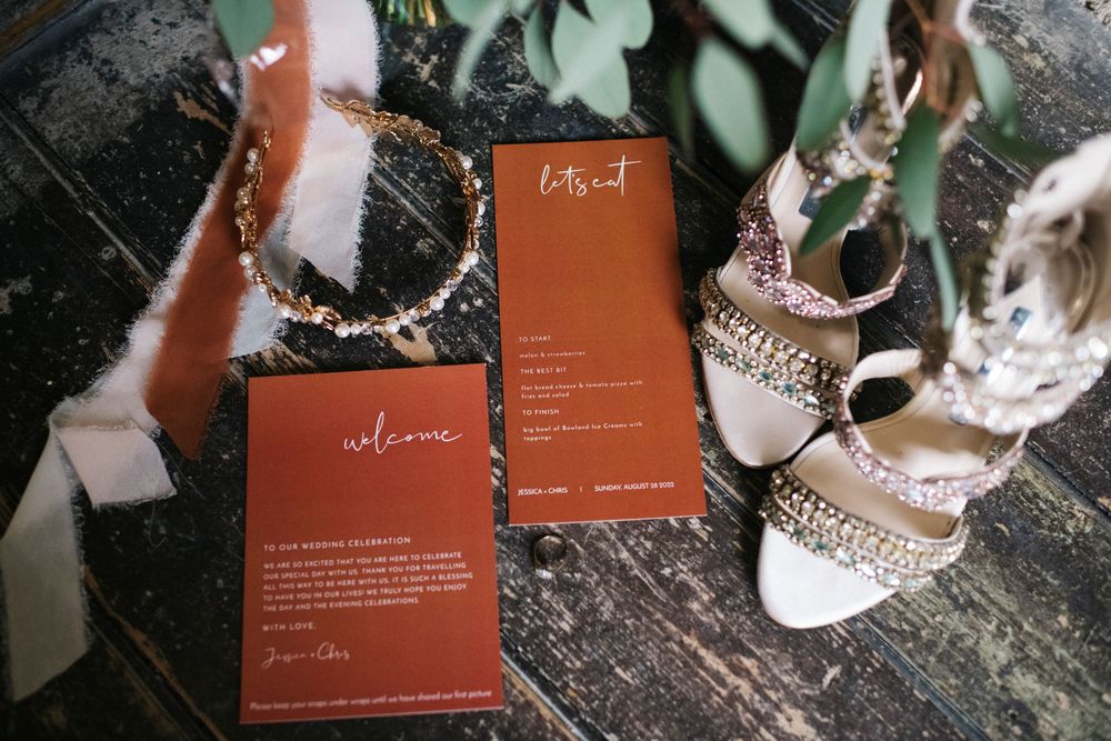 Terracotta colored wedding stationery displayed on dark wooden surface with botanical elements.