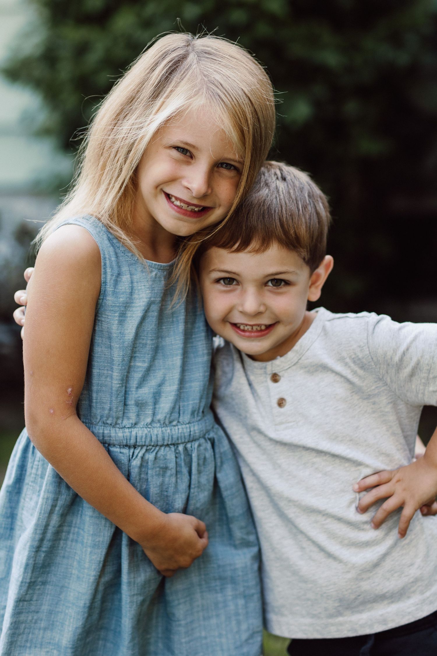 Two children in casual clothing smiling together outdoors.