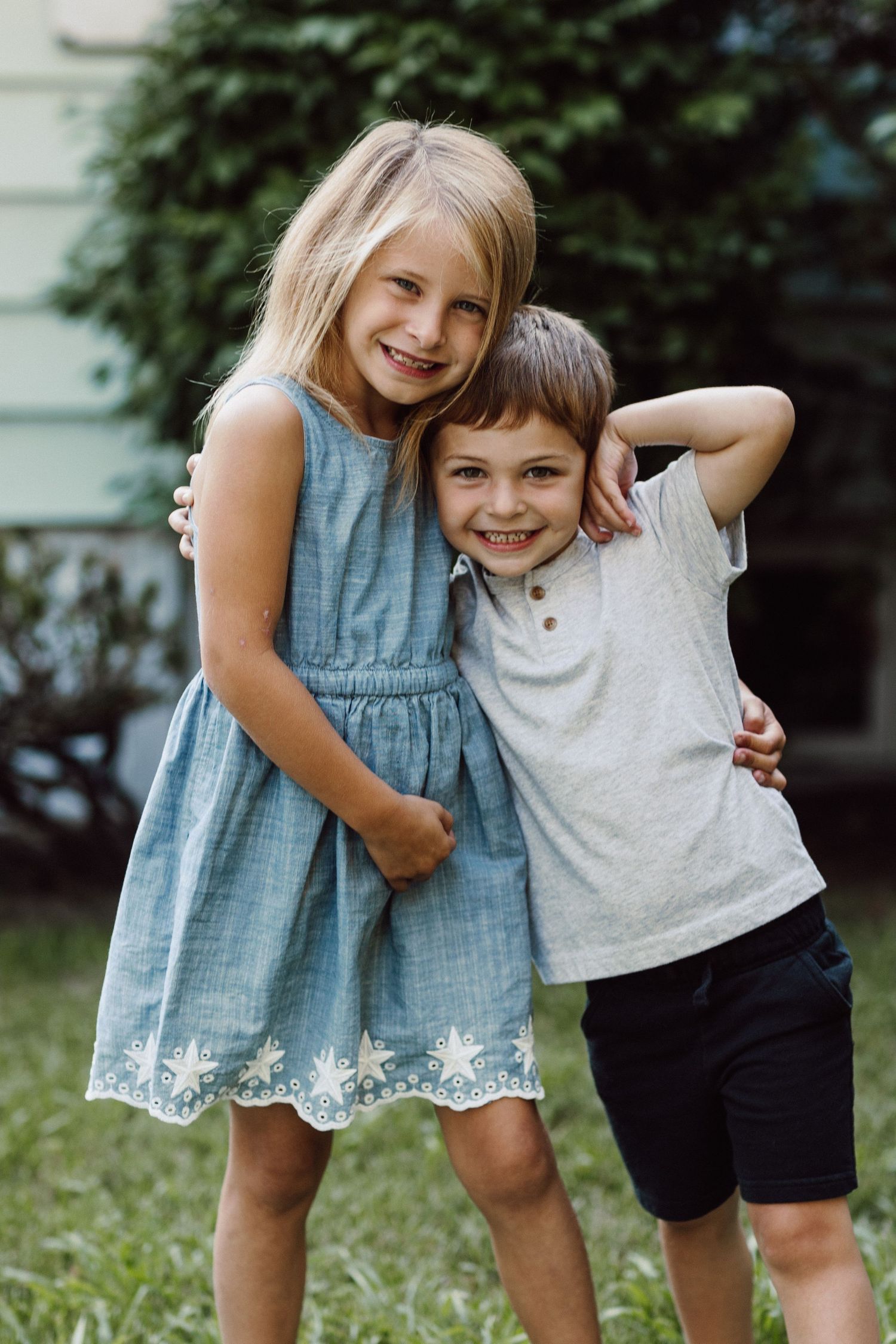 Two children in summer clothes posing playfully together outside.