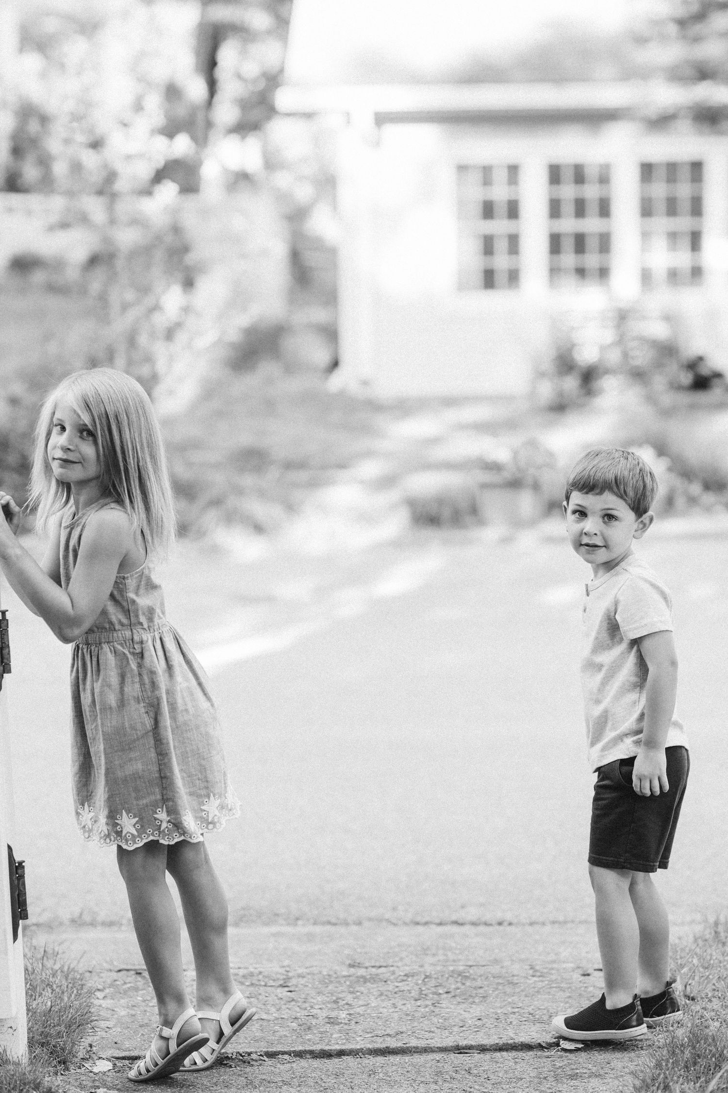 Black and white photo of two children playing near a white house on a sunny day.