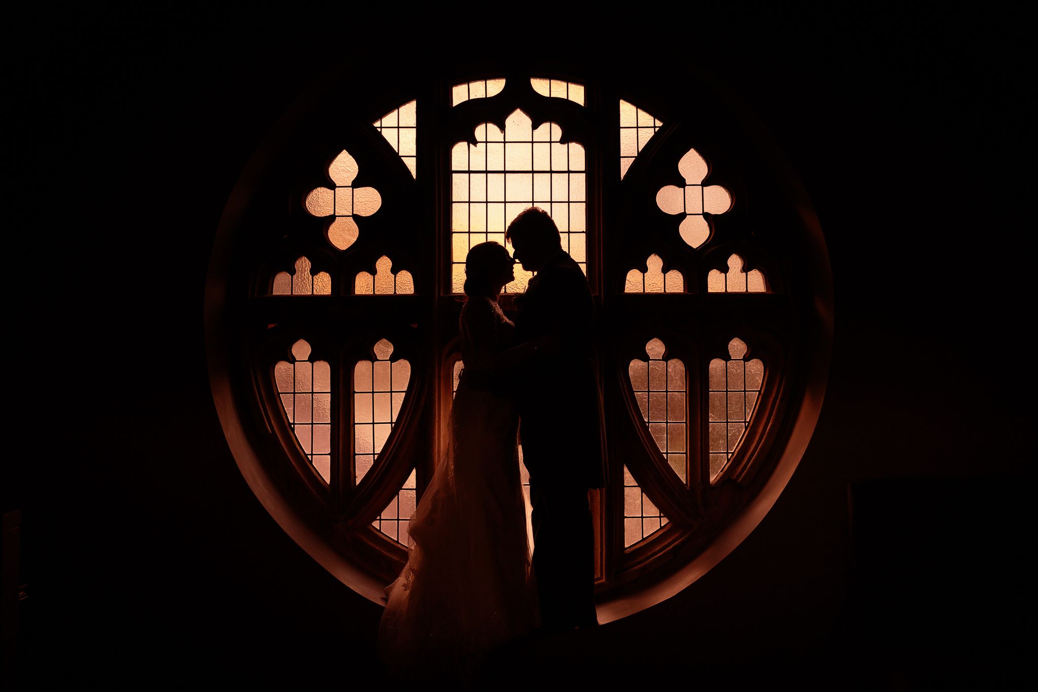 Dramatic backlit scene through decorative circular chapel window. Ellingham Hall