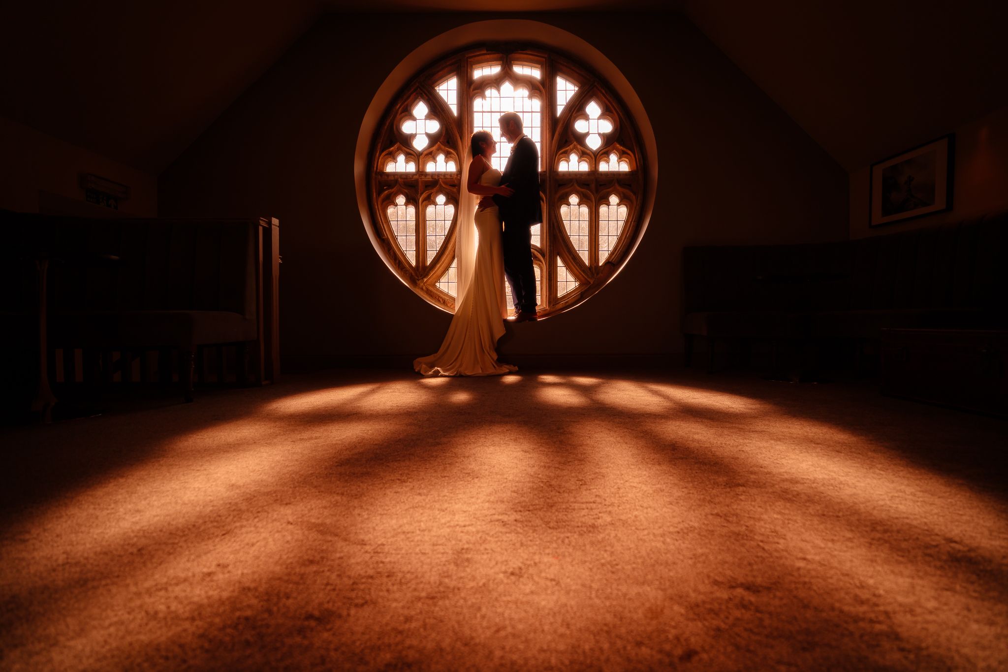 Ornate round church window casting warm light patterns on floor. Ellingham Hall