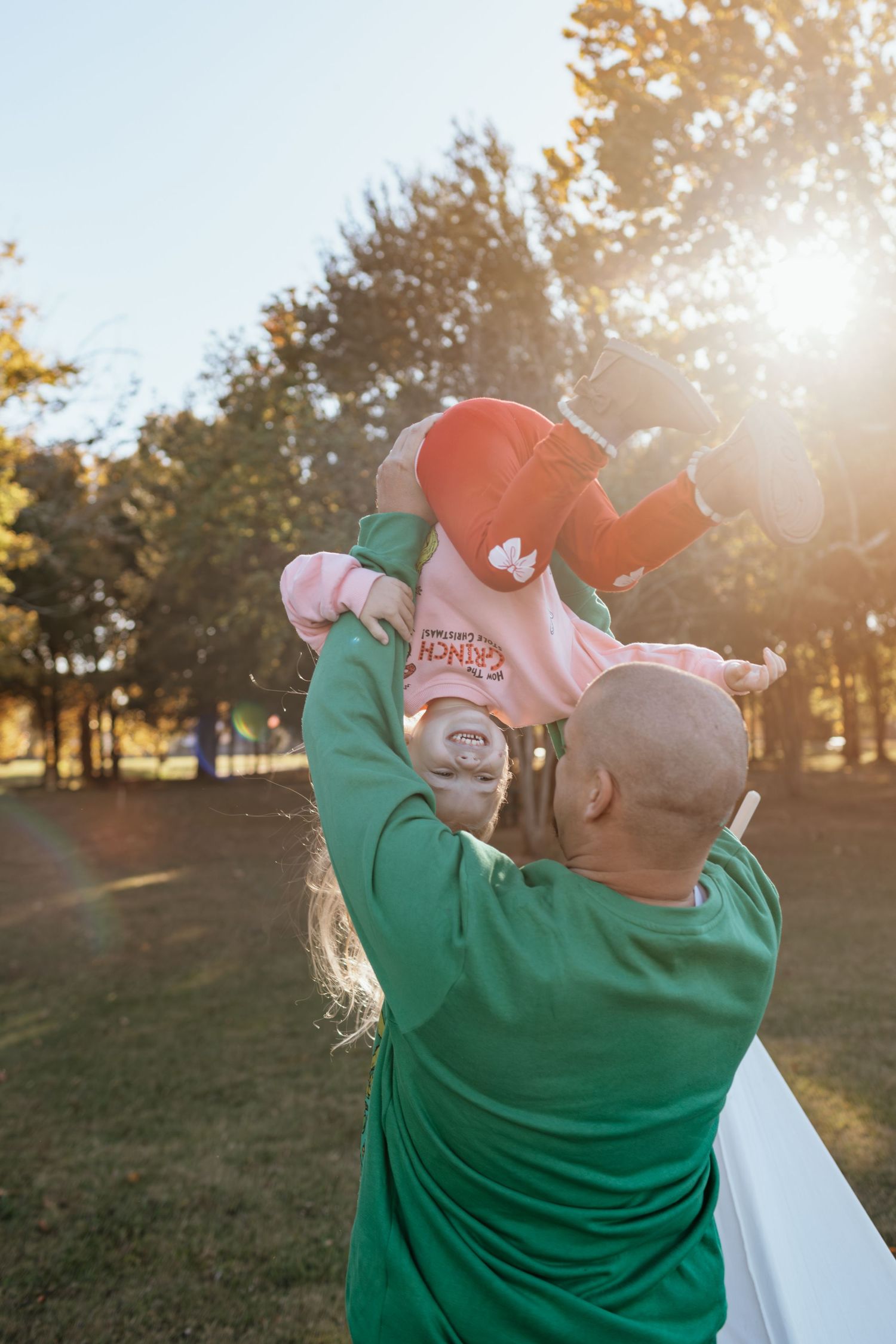 A couple in casual attire embraces outdoors during golden hour sunset in a grassy park setting.