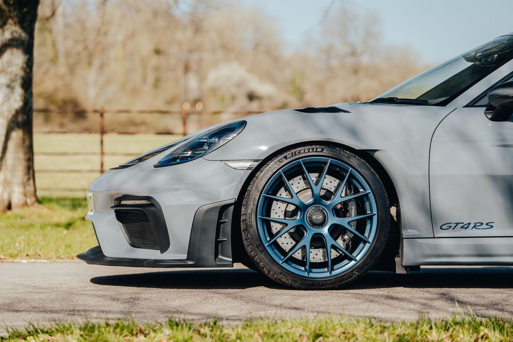 A silver sports car with blue-accented wheels parked on a paved surface in outdoor lighting.