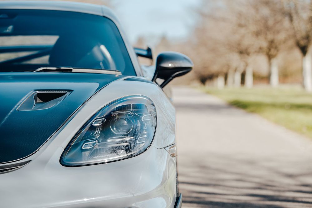 Close-up view of a silver Porsche sports car headlight and front quarter panel on a sunny day.