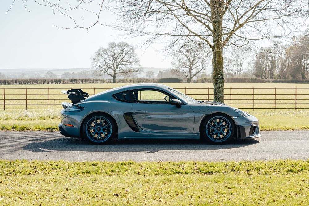 Side profile of a sleek Porsche sports car parked on a rural road with trees in the background.