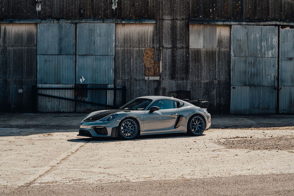Sleek silver Porsche 918 Spyder supercar parked in front of industrial concrete wall in dramatic lighting.