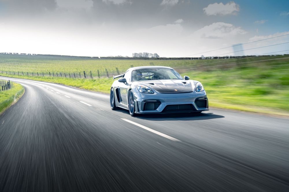Light blue McLaren hypercar racing on a winding road with green hills and dramatic sky in the background.