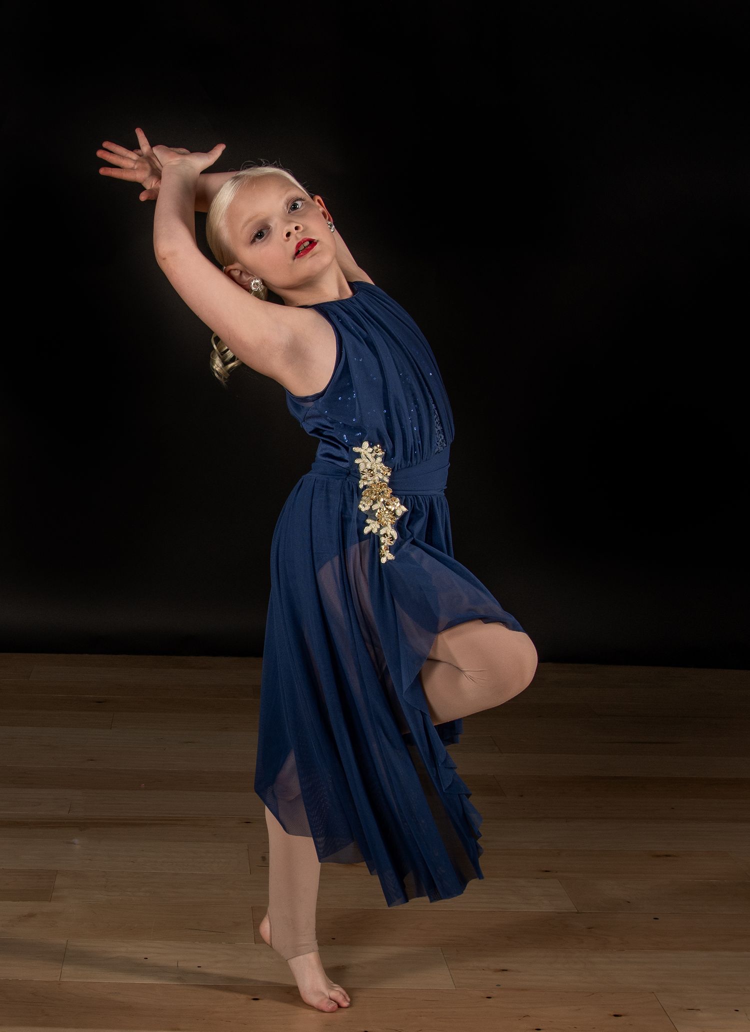 A graceful dancer in a flowing mauve dress performs an elegant leap against a dark background.