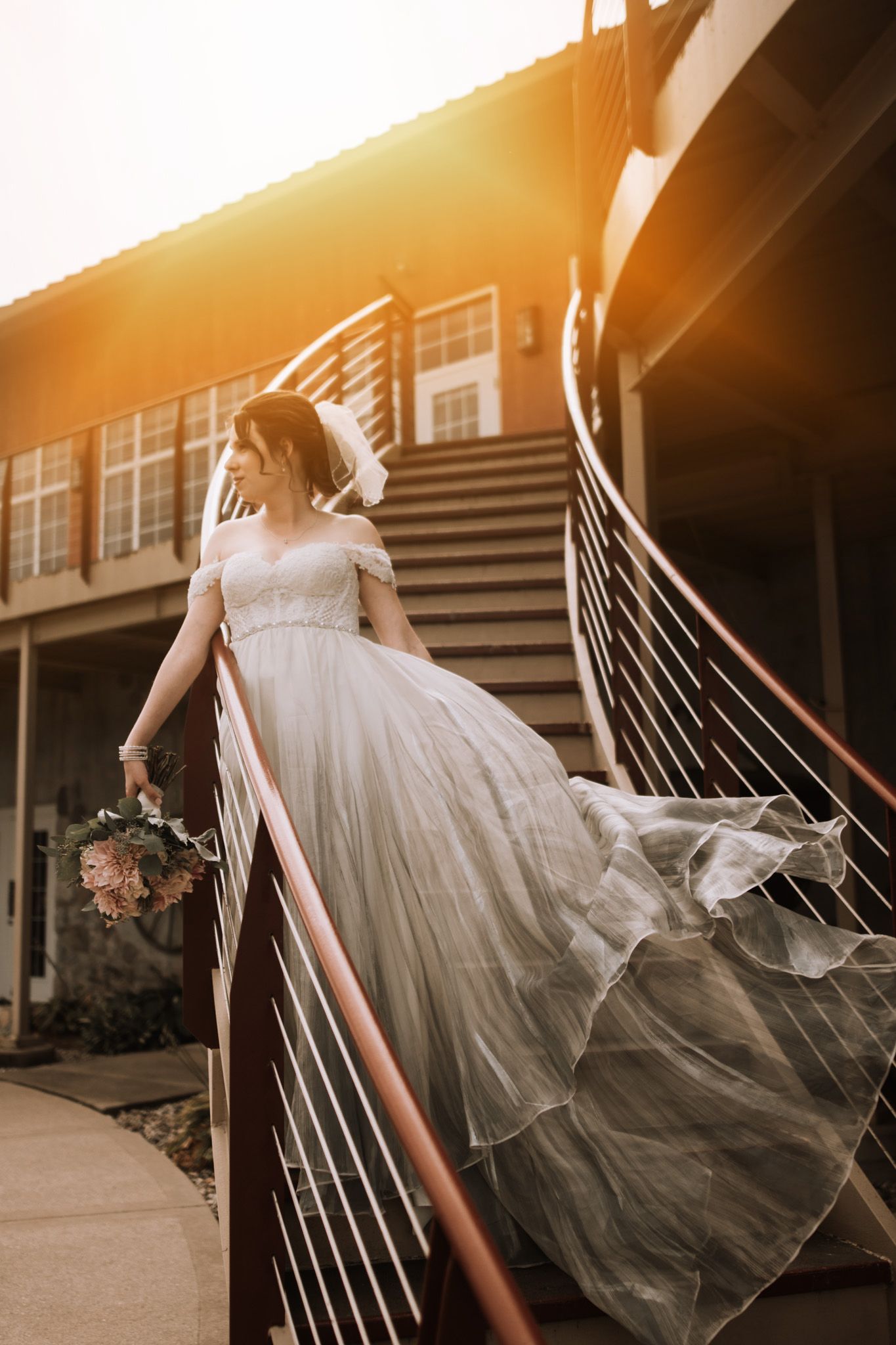 A flowing white tulle wedding dress captured in motion against warm sunset lighting on outdoor stairs.