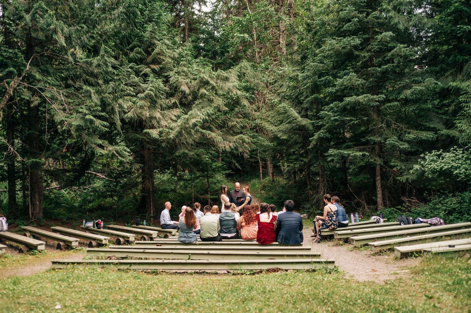 Avalanche amphitheater wedding in Glacier National Park, guests seated in rows among tall evergreen trees in an outdoor forest setting.