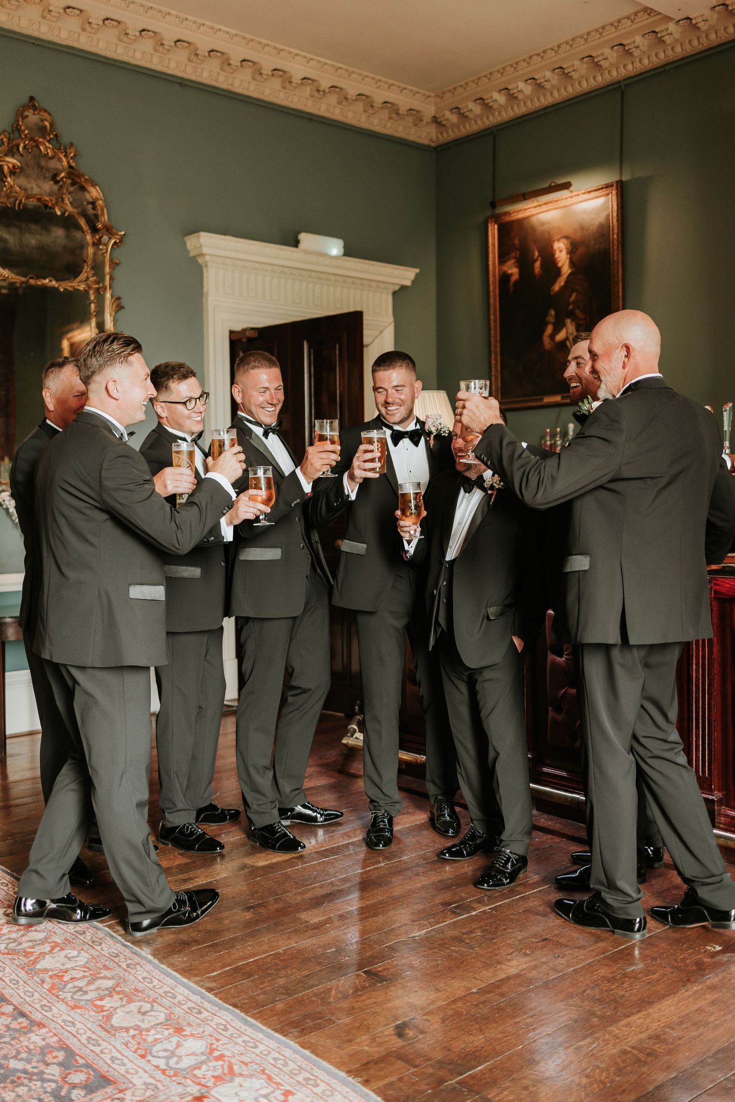 A sequence of wedding party members in black tuxedos taking shots together in an elegant room with ornate molding.