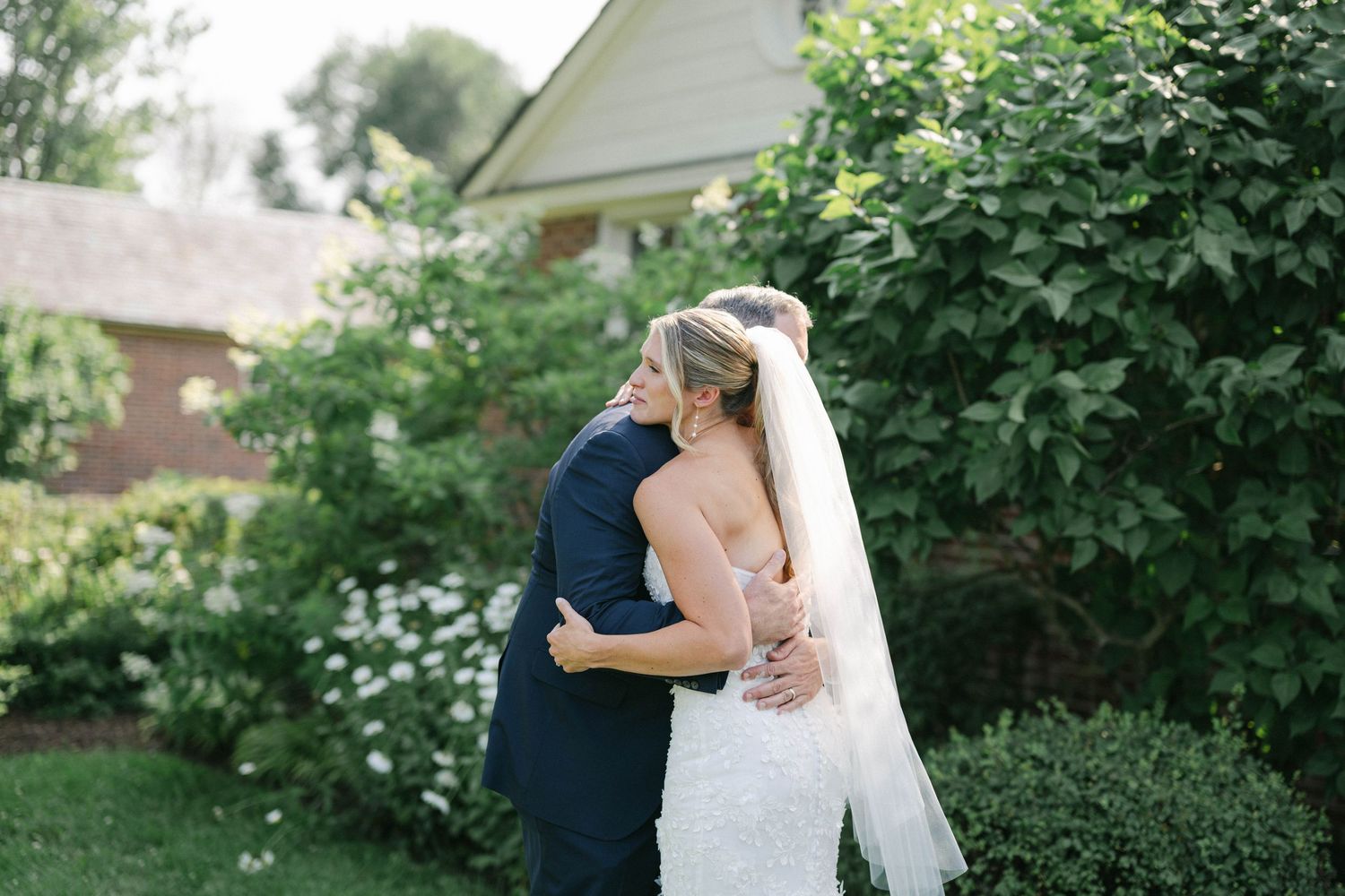 A couple in wedding attire embraces in a lush garden setting during a romantic outdoor photo session. - Elawa Farm