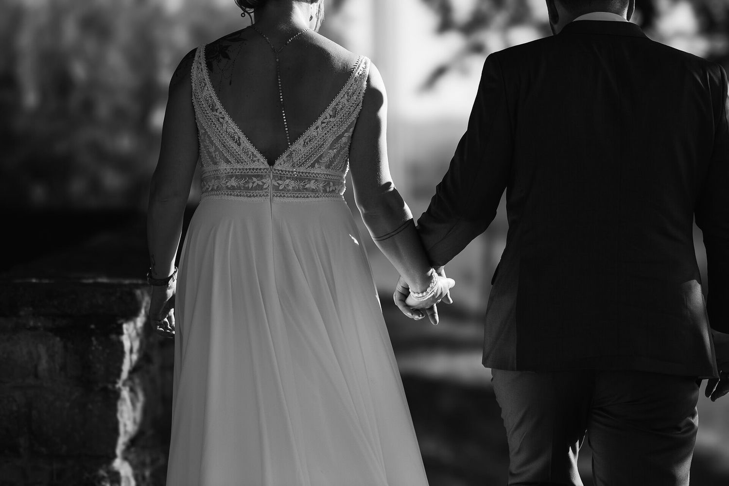 Black and white photo of a couple holding hands, with focus on wedding dress and suit details.