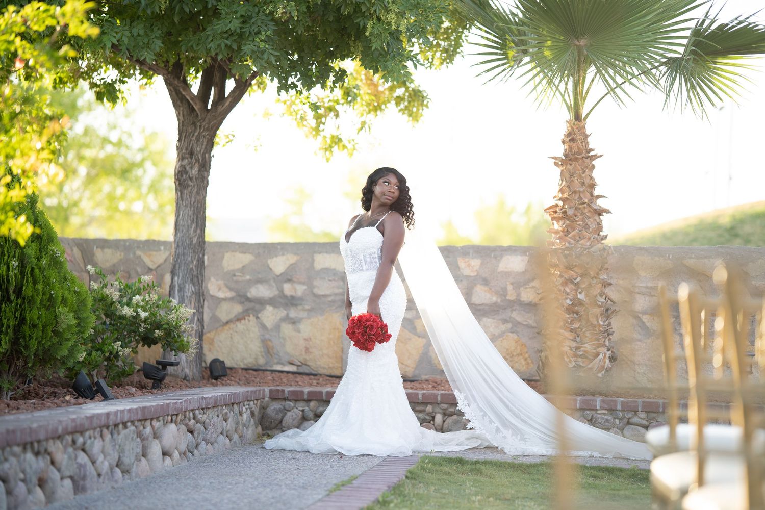 Wedding attendants walk down the aisle outdoors, with the bridesmaid carrying vibrant red flowers.