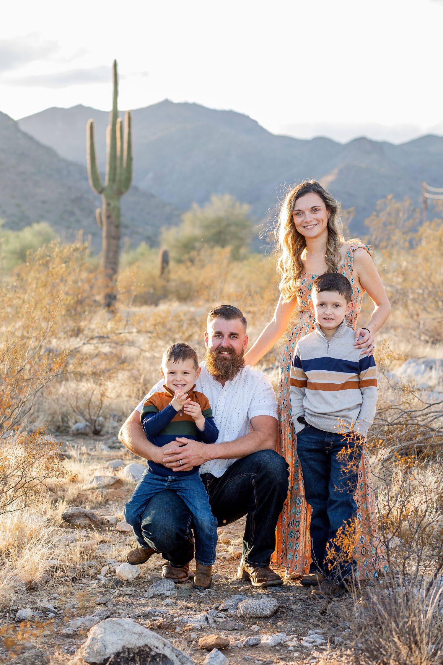 Family of four posing in Sonoran Desert with saguaro cactus and mountains at golden hour.