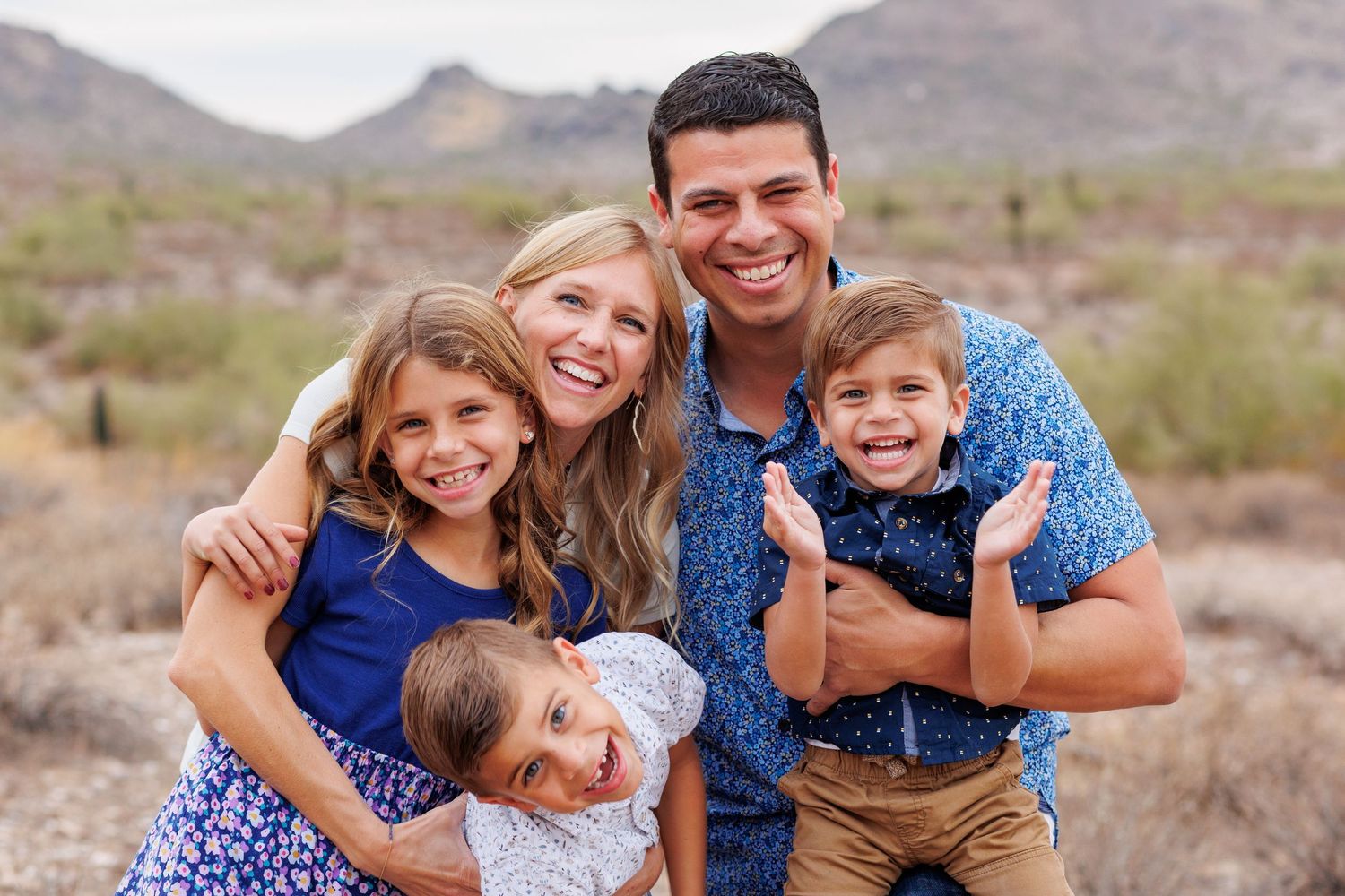 Happy family of five smiling together in Arizona desert landscape with mountains in background.