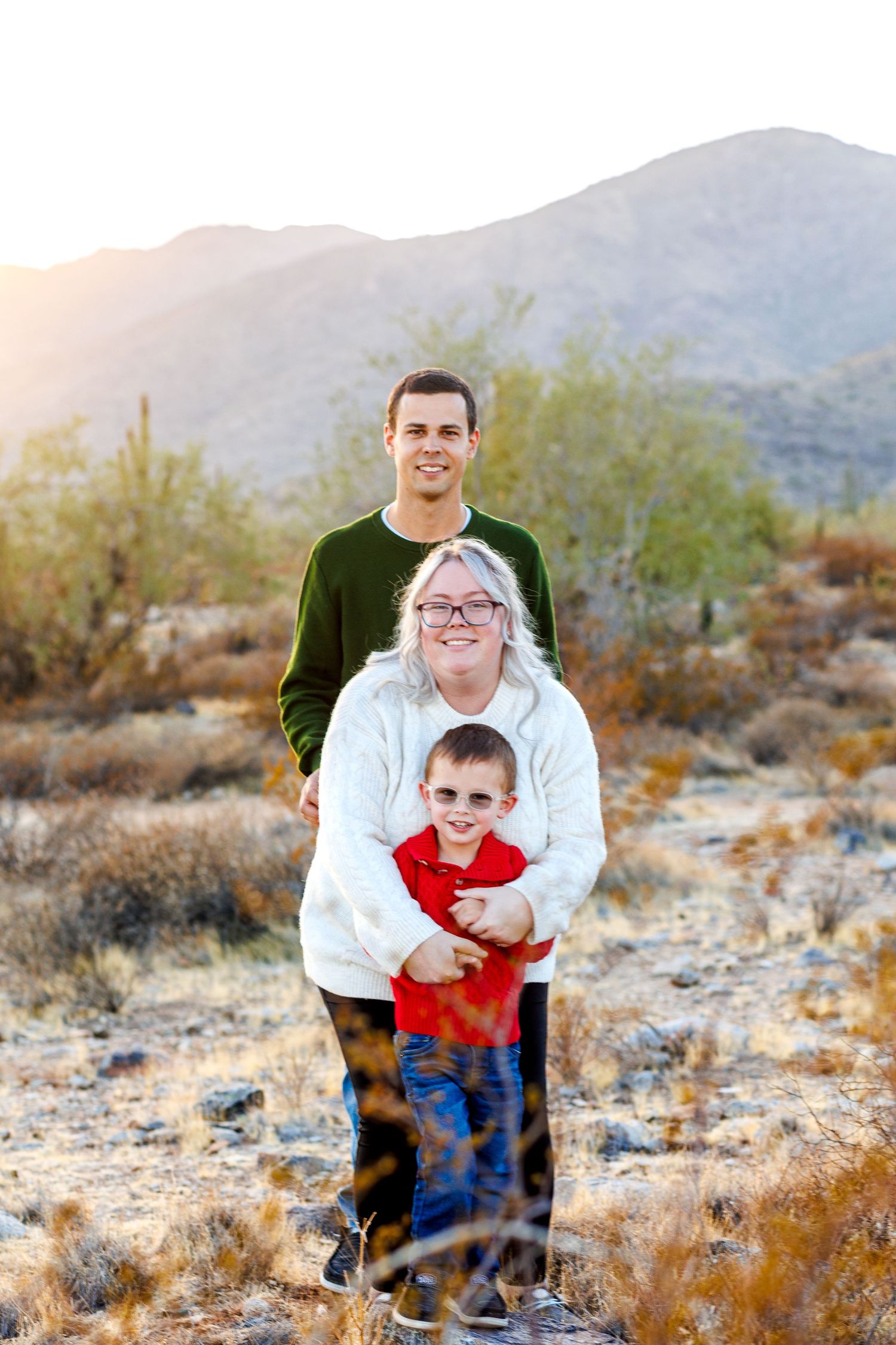 Family of three posing together at sunset in desert landscape with mountain and saguaro cactus backdrop.