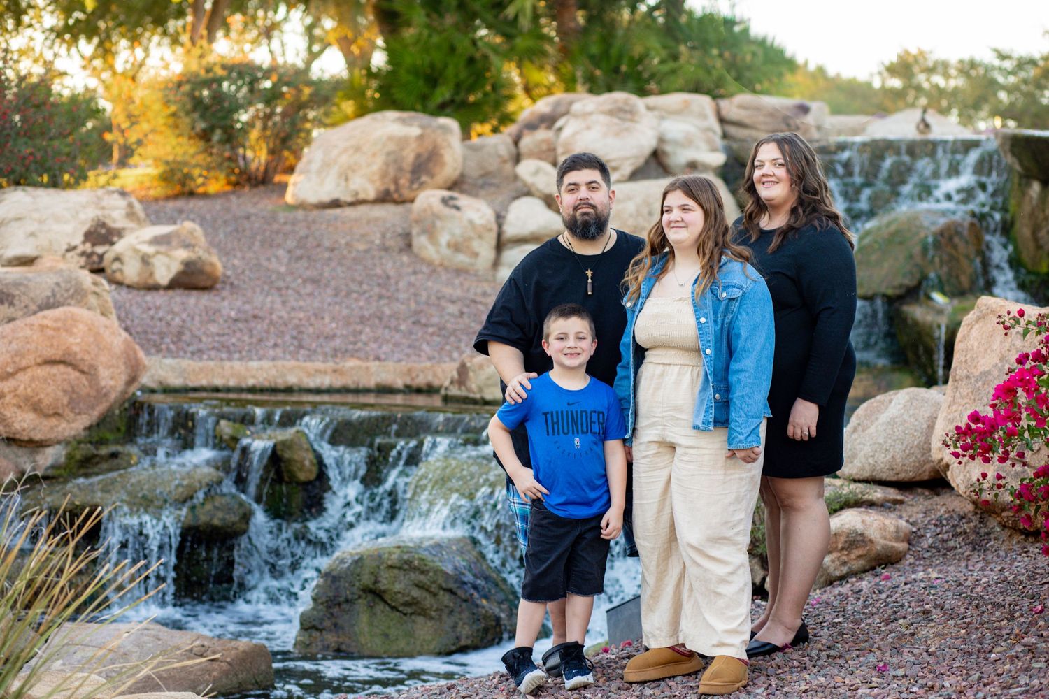 Family of four posing by rocky waterfall outdoors, including two adults and two children in casual attire.
