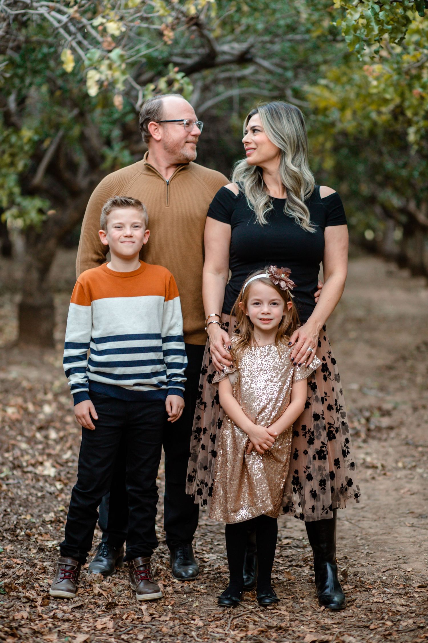 Family of four posing in wooded autumn setting with children in festive holiday outfits.