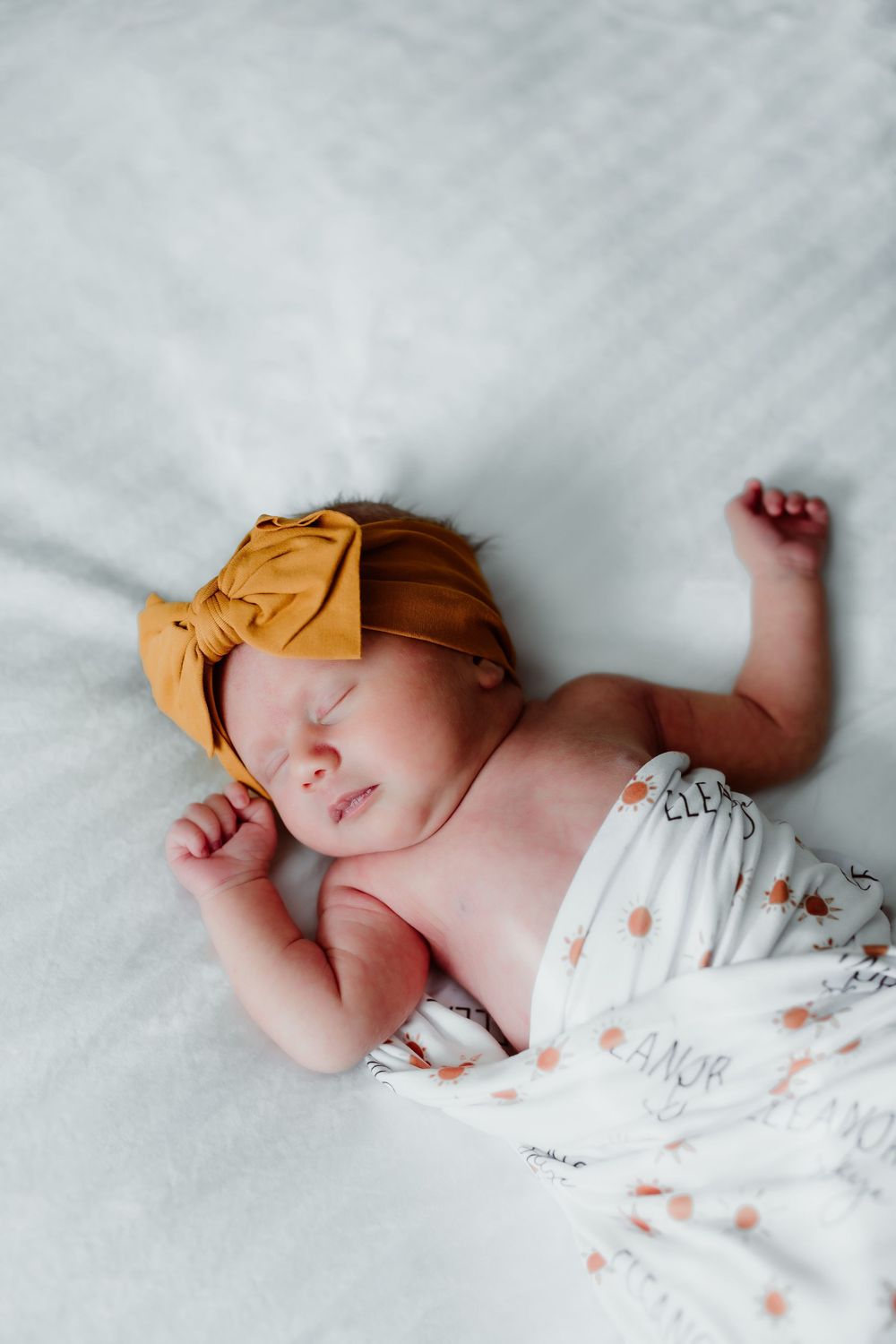 Sleeping baby wearing yellow headband on white textured bedding.