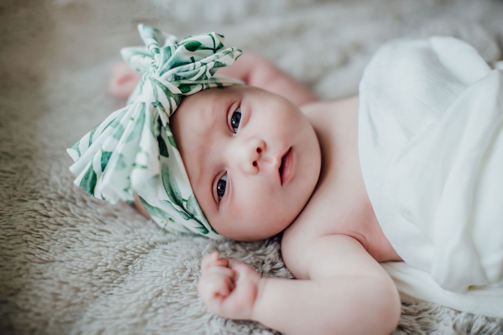 Baby in mint green headband lying on soft carpet.