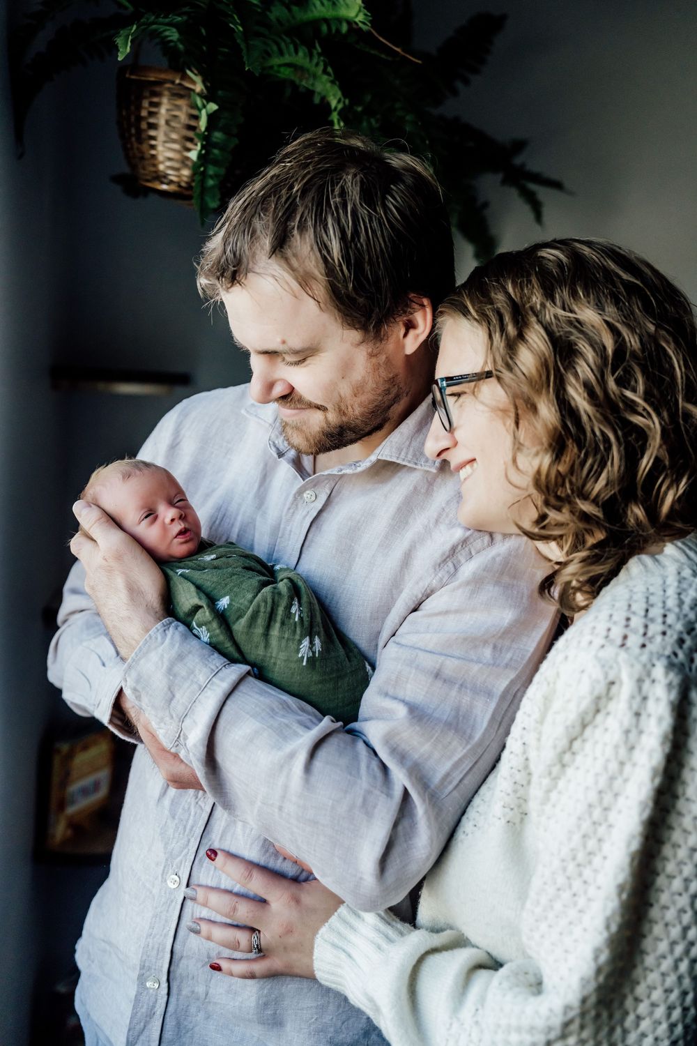 Tender family moment captured in natural light with soft knit textures and indoor plants.