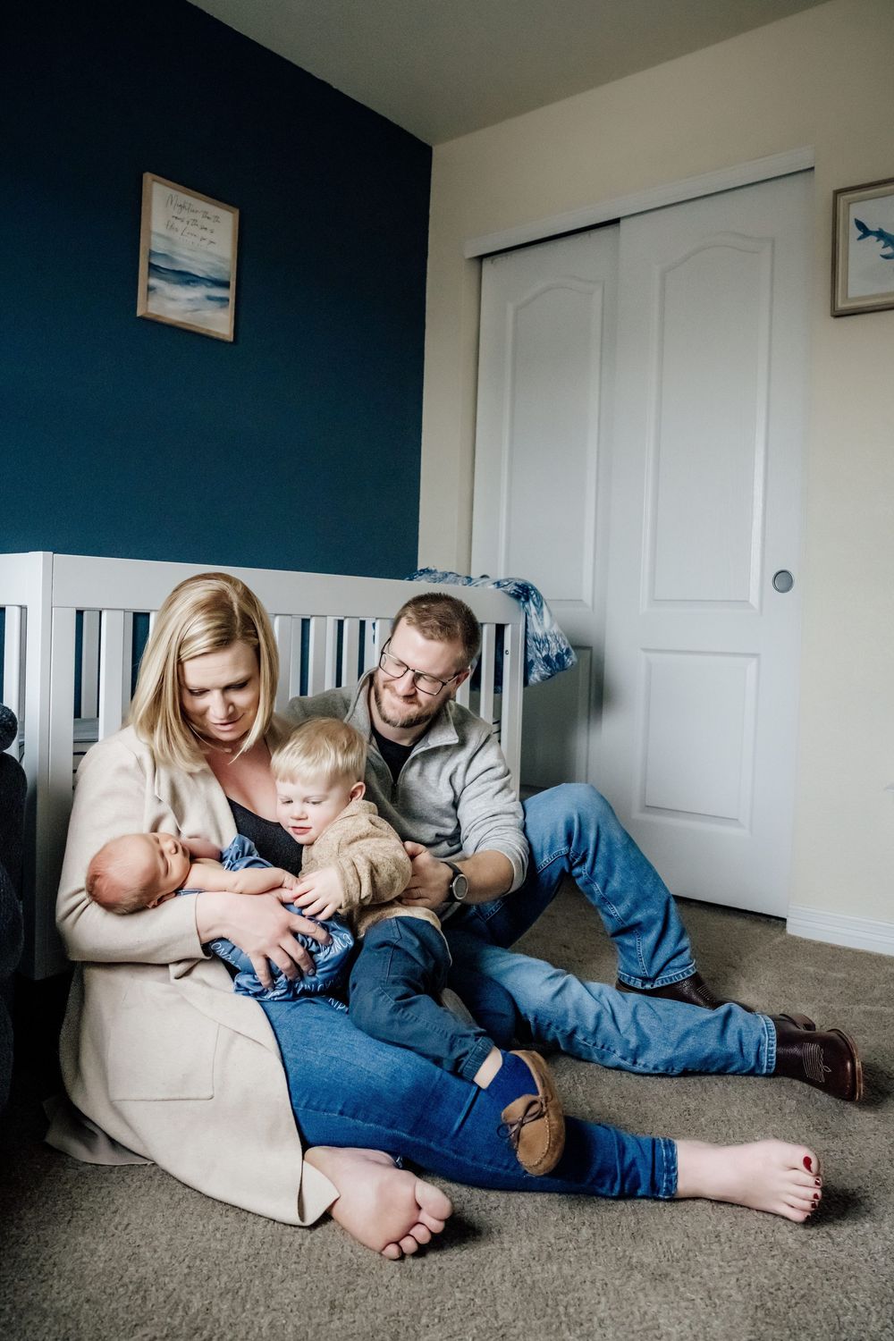 Family lounging together on beige carpet against navy blue wall in casual home setting.