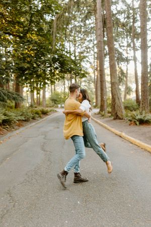 Playful couple dancing and spinning on a tree-lined path during golden hour.