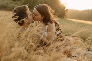 Romantic couple embracing on grassy hillside during golden hour sunset.