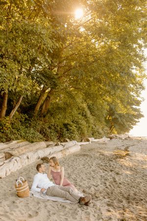Couple lying on sandy beach at sunset surrounded by trees and golden light.