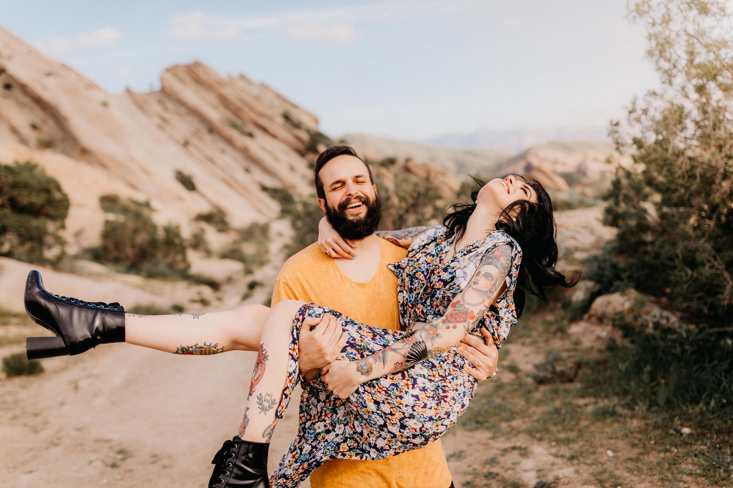 A couple shares a romantic moment in a desert landscape with golden sunlight and rocky terrain.