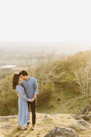 Couple sharing an intimate moment on a hilltop during golden hour with misty background.