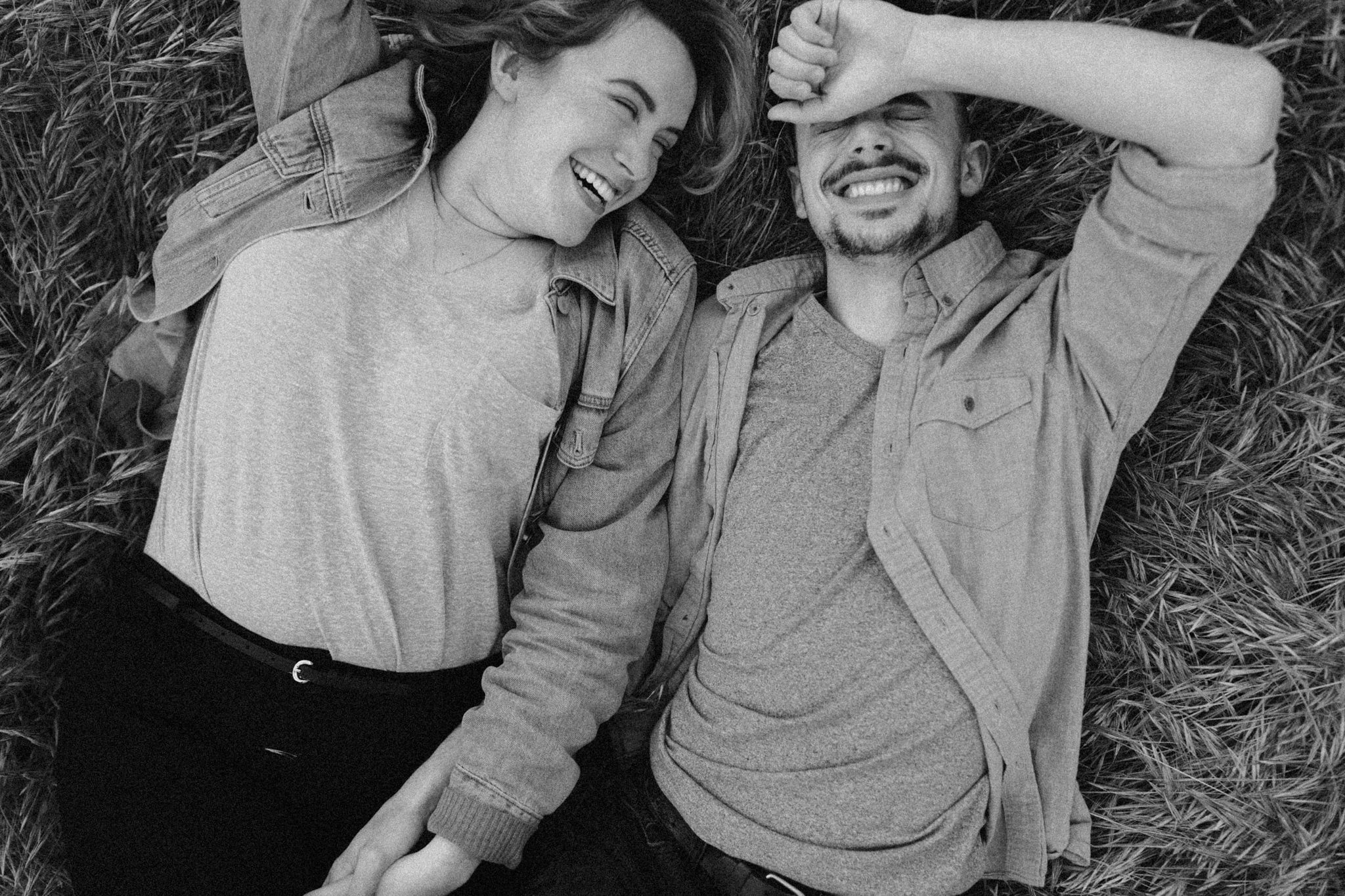 Two people lying in grass sharing a candid laughing moment together.