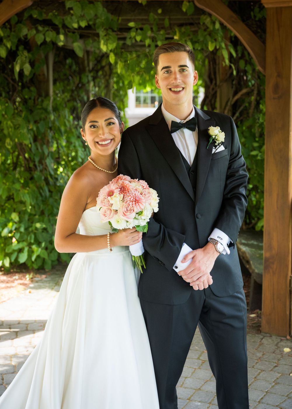 Wedding couple poses together under a rustic wooden pergola with green vines during outdoor photo session.