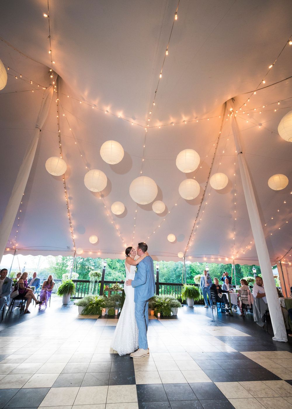 A wedding reception venue decorated with string lights and paper lanterns creating a romantic atmosphere on a covered patio.
