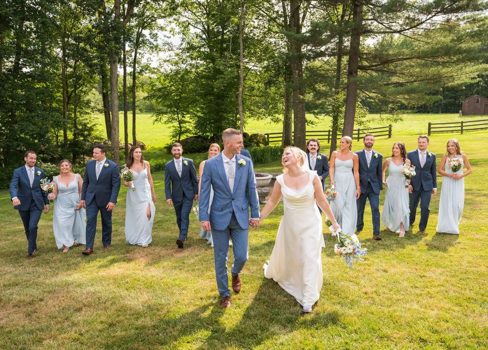 Wedding party walks together across a sunny green lawn during an outdoor summer celebration.