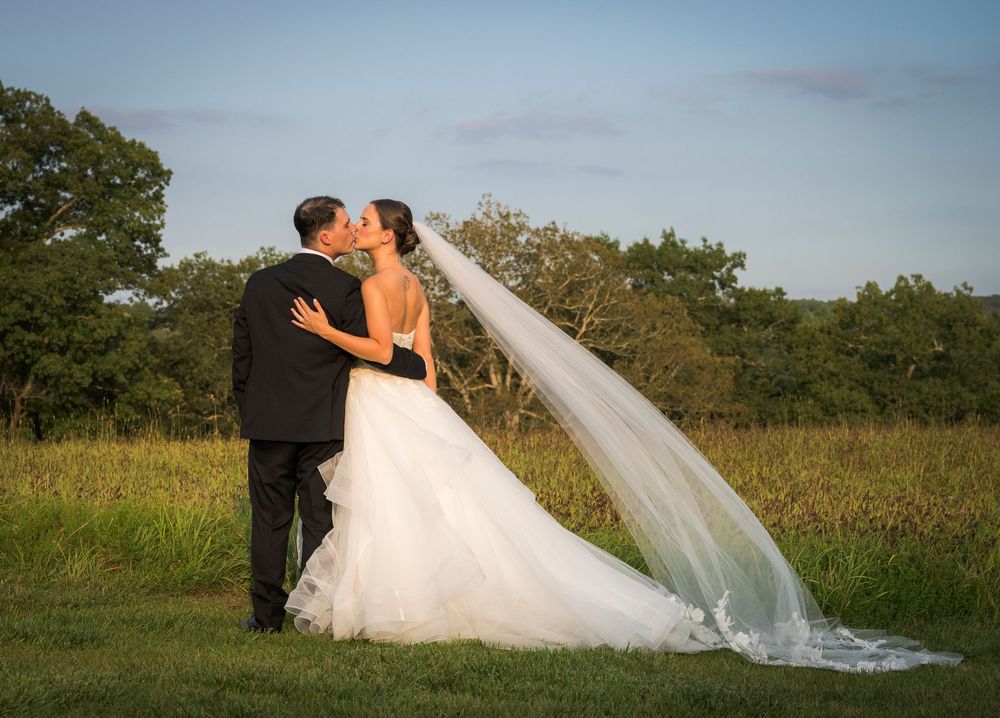 A romantic wedding photo series showing a couple in a field with a flowing veil at sunset.