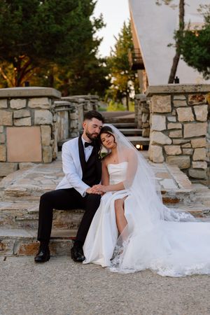 A wedding couple sits together on stone steps during sunset at an outdoor venue.
