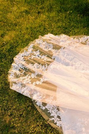 Detail shot of delicate lace trim on white wedding dress train laying on grass.