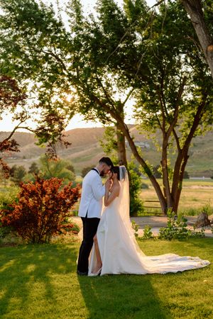 A romantic sunset wedding photo of a couple embracing on a lush lawn with rolling hills in the background.