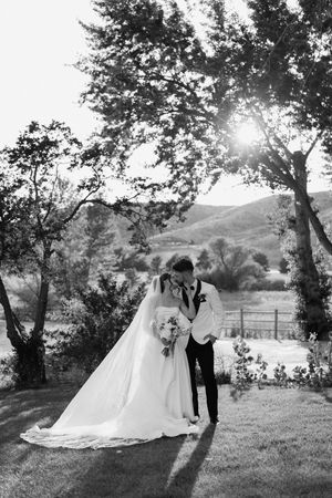A wedding couple poses in a scenic garden setting with mountains and trees in the background.