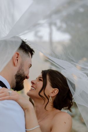 A romantic wedding moment captured under a flowing veil as the newlyweds share an intimate embrace.