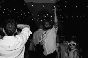 A black and white photo showing people dancing at a party with raised arms and silhouettes against a dark background.